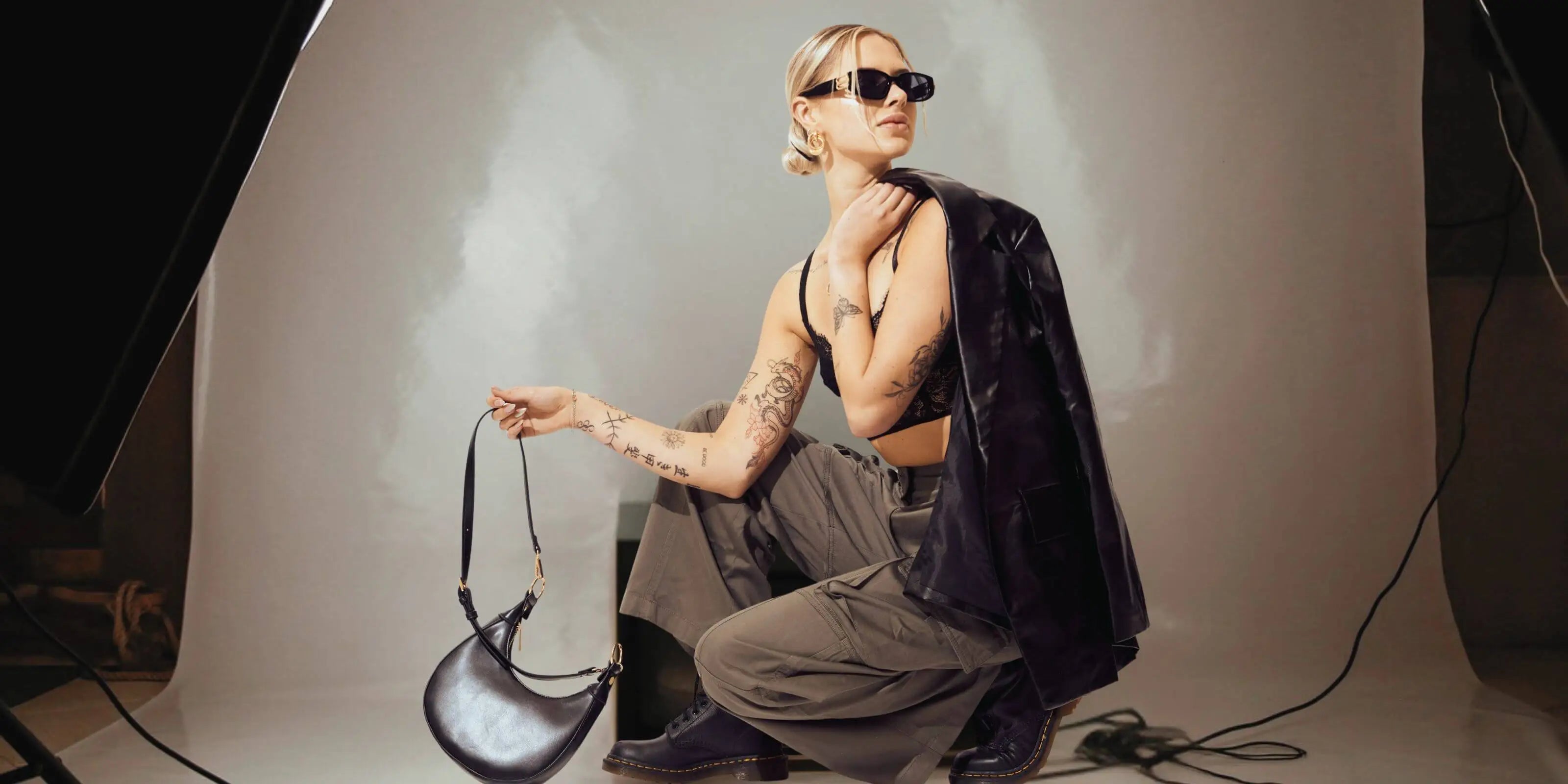 Person posing with a handbag in a studio setting holding leather jacket with unique style