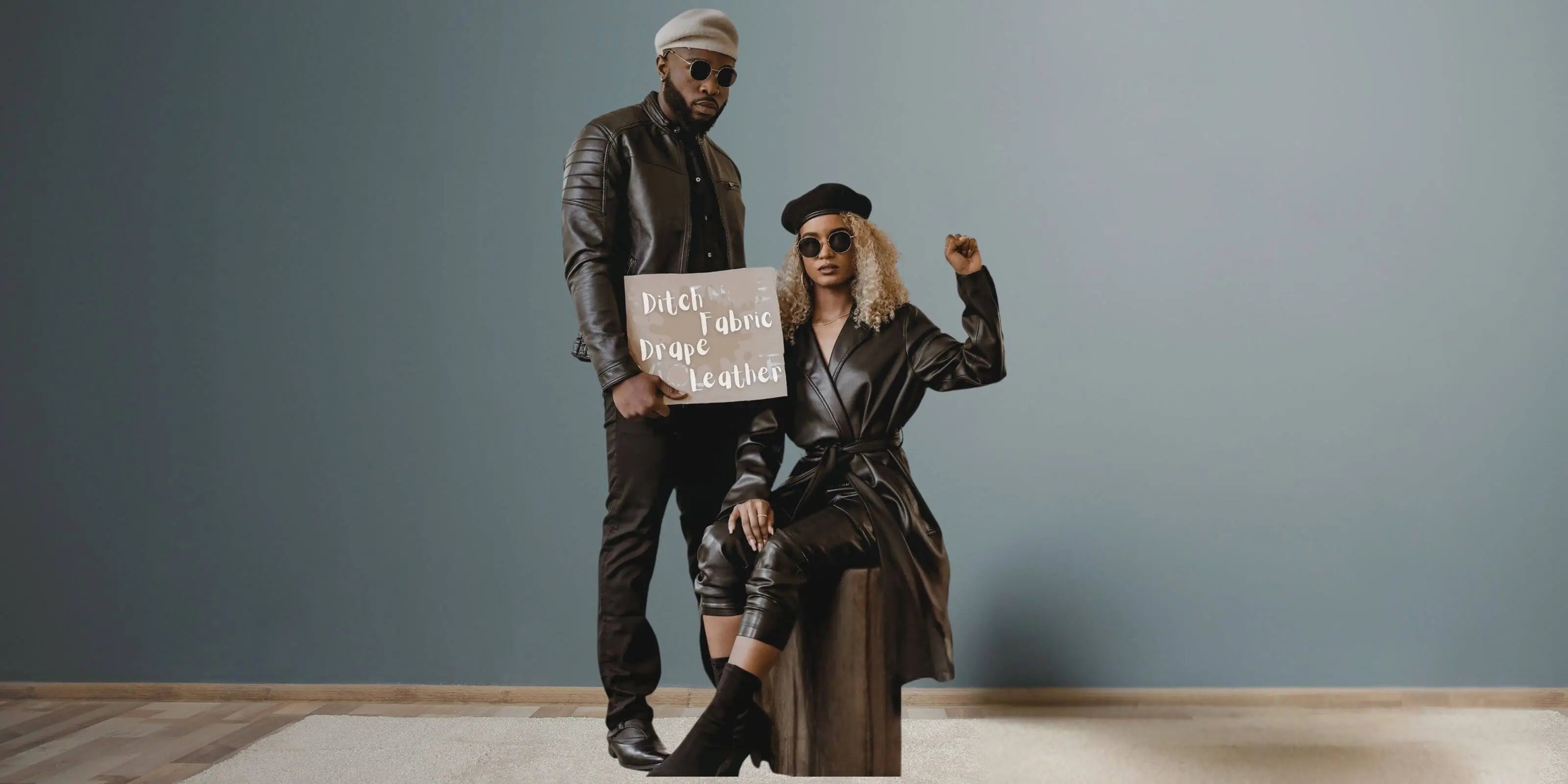 Two people in stylish outfits holding a sign against a plain background